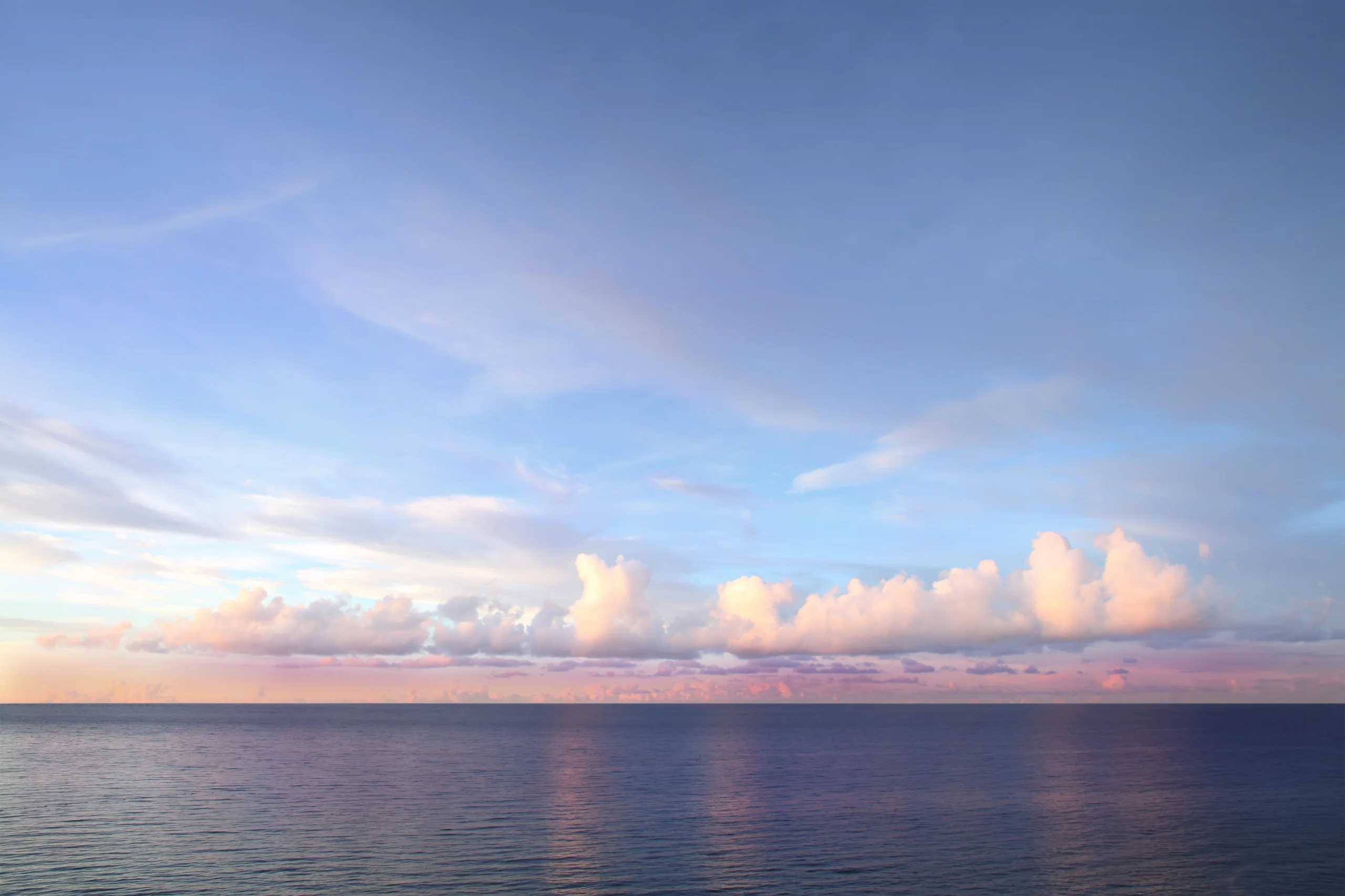 Horizonte de mar en calma al atardecer, con nubes bajas teñidas de rosa.